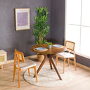 A solid oak round dining table with wooden butterfly legs, placed on a round white rug in a room with a gray wall and wooden floor.